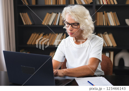 Confident stylish middle aged senior woman using laptop at workplace. Older mature lady businesswoman sitting at office table with laptop and paper document. Boss leader teacher professional worker Confident stylish middle aged senior woman using laptop at workplace. Older mature lady businesswoman sitting at office table with laptop and paper document. Boss leader teacher professional worker 123466143