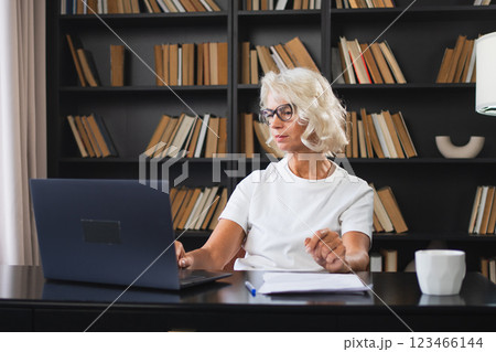 Confident stylish middle aged senior woman using laptop at workplace. Older mature lady businesswoman sitting at office table with laptop and paper document. Boss leader teacher professional worker Confident stylish middle aged senior woman using laptop at workplace. Older mature lady businesswoman sitting at office table with laptop and paper document. Boss leader teacher professional worker 123466144