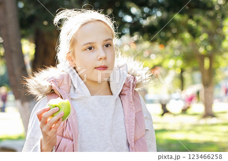 Cheerful young girl eating green apple outdoors, portrait. Child 11 years old Cheerful young girl eating green apple outdoors, portrait. Child 11 years old 123466258