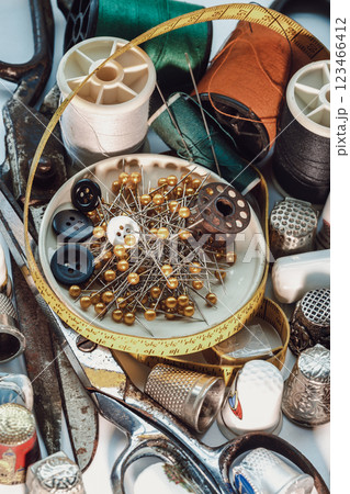 Sewing needles stuck in a green miniature spools thread Steel scissors, Spools of thread of various colour, Thimbles and Measuring tape including Pins and Buttons in small round tray. 123466412