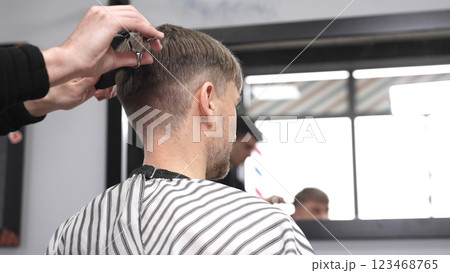 Professional barber cutting hair of male client with clipper, creating precise contemporary hairstyle in modern grooming environment 123468765