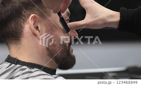 Professional barber performing precise beard shaving with classic straight razor, working in modern barbershop with skilled grooming technique Professional barber performing precise beard shaving with classic straight razor, working in modern barbershop with skilled grooming technique 123468849