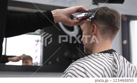 Professional barber trimming male client's hair using electric razor, creating precise haircut in contemporary barbershop setting with sleek styling tools 123468850