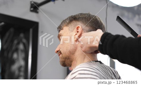 Professional barber carefully combing client's hair, preparing precise haircut in stylish barbershop, delivering contemporary men's grooming service 123468865