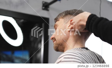 Professional barber carefully combing client's hair, preparing precise haircut in stylish barbershop, delivering contemporary men's grooming service Professional barber carefully combing client's hair, preparing precise haircut in stylish barbershop, delivering contemporary men's grooming service 123468898