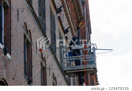 Worker cleaning the window of a building at heigt in lifting cradle. Construction workers at height working on crane in lifting bucket. Worker cleaning the window of a building at heigt in lifting cradle. Construction workers at height working on crane in lifting bucket. 123470510