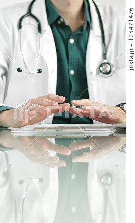 Doctor man wearing a stethoscope and lab coat is gesturing with hands while explaining a diagnosis to a patient across a glass desk with a laptop. Medicine concept 123471476