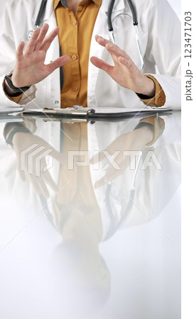 Unknown male doctor wearing a stethoscope, yellow shirt under a lab coat is gesturing with hands overs a glass desk with a laptop in clinic office. Medicine concept 123471703