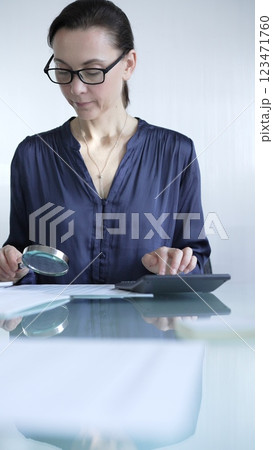 Woman accountant examining financial documents with magnifying glass at glass office desk, conducting thorough analysis of business transactions. Audit and taxes in business Woman accountant examining financial documents with magnifying glass at glass office desk, conducting thorough analysis of business transactions. Audit and taxes in business 123471760