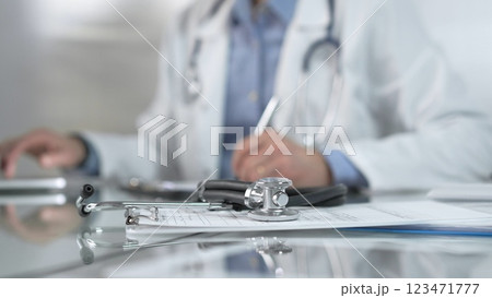 Stethoscope and medication history records form are on a glass table before a male doctor working with laptop in clinical office background. Medicine concept Stethoscope and medication history records form are on a glass table before a male doctor working with laptop in clinical office background. Medicine concept 123471777