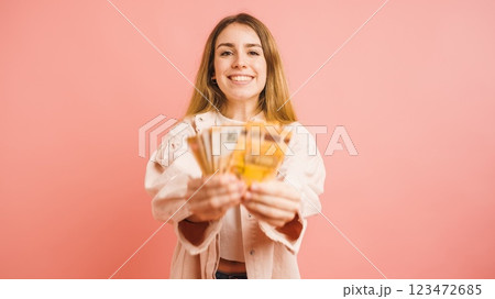 Smiling young woman showing euro banknotes on pink background Smiling young woman showing euro banknotes on pink background 123472685