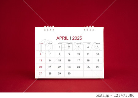 April 2025 white desk calendar stand on dark red background. April 2025 white desk calendar stand on dark red background. 123473396