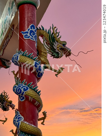 Dragon sculpture, artistically designed with vibrant colors, stands on a pillar against a stunning sunset. Dragon sculpture, artistically designed with vibrant colors, stands on a pillar against a stunning sunset. 123474019