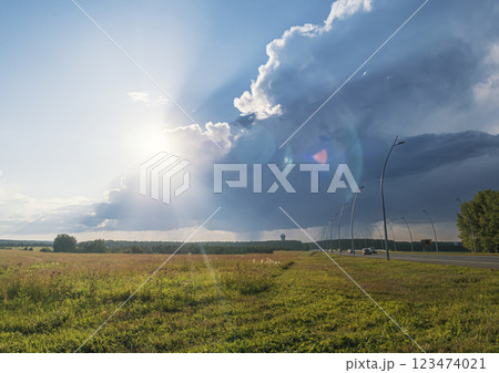 Dramatic cloud formations over a vast grassy field during sunset near a winding road in the countryside 123474021