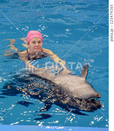 Woman swims alongside dolphin in clear blue water during marine interaction session at aquatic facility 123474165