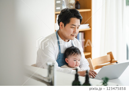 0歳児の赤ちゃんを抱っこしながらパソコンを見るパパ 123475858