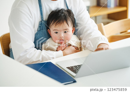 テレワークをするパパの膝に座る0歳児の赤ちゃん テレワークをするパパの膝に座る0歳児の赤ちゃん 123475859