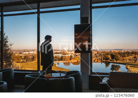 successful man by window of golf club looking at serene lake from modern indoor space during sunset successful man by window of golf club looking at serene lake from modern indoor space during sunset 123476060