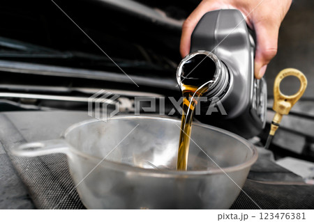 The mechanic poured engine oil into a funnel on the engine oil fill port The mechanic poured engine oil into a funnel on the engine oil fill port 123476381
