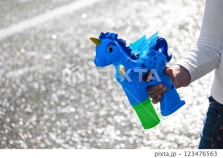 Close-up of a child's hand holding a blue unicorn-shaped bubble gun against a sparkling festive background. Concept: childhood, playfulness, fun Close-up of a child's hand holding a blue unicorn-shaped bubble gun against a sparkling festive background. Concept: childhood, playfulness, fun 123476563