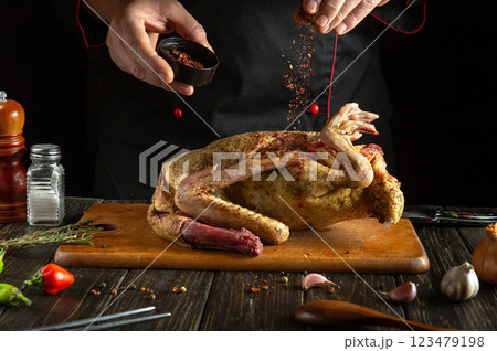 Sprinkling dry spices on a raw duck carcass before cooking in the kitchen. The chef uses his hands to add aromatic seasonings to the bird on the cutting board. A delicious roast duck dinner. 123479198