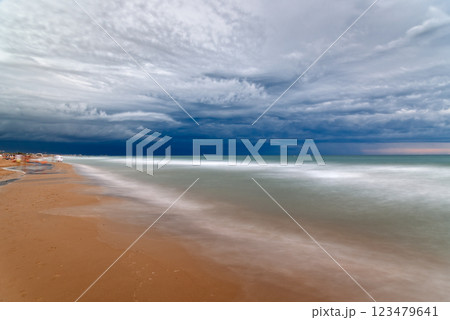 Dramatic clouds hover above the ocean waves gently washing onto the sandy beach shore. Dramatic clouds hover above the ocean waves gently washing onto the sandy beach shore. 123479641