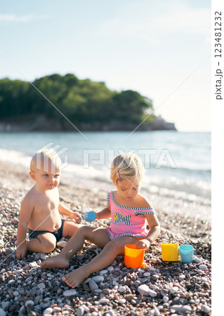 Little boy and girl with toy molds on a pebble beach. High quality photo 123481232