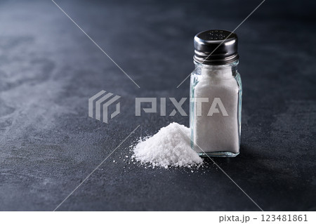 salt shaker with crystals of salt on a black stone table, selective focus. 123481861