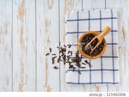 wooden bowl with cloves spice on a white wooden table, top view. 123482006
