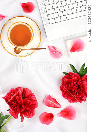 A cozy home table with a laptop, smartphone,tea and a bouquet of delicate peonies and roses. A gift for loved ones and congratulations on the holiday. The concept of working from home online 123482420