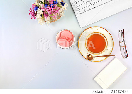 Modern feminine desk, home office. Computer, hyacinth flowers and a cup of tea, macaroons on an elegant table, lifestyle concept, comfortable work from home, template for design, flat lay 123482425