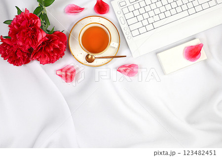 A cozy home table with a laptop, smartphone, tea and a bouquet of delicate peonies and roses. A gift for loved ones and congratulations on the holiday. The concept of working from home online, sunny 123482451