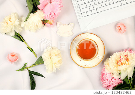 Concept of working from home online. Cozy home desk with laptop, smartphone, tea and a bouquet of delicate peonies and roses. Gift for loved ones and congratulations on the holiday, sunny good 123482462