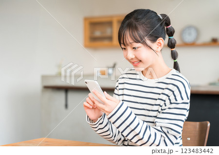 自宅のリビング・ダイニングでスマホを使う小学生・中学生の女の子 自宅のリビング・ダイニングでスマホを使う小学生・中学生の女の子 123483442