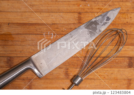 A large kitchen knife and a metal whisk placed on a wooden cutting board. A large kitchen knife and a metal whisk placed on a wooden cutting board. 123483804