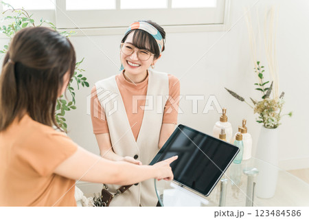 美容室・ヘアサロンで電子書籍・タブレットのヘアカタログを見る女性と美容師・スタイリスト 美容室・ヘアサロンで電子書籍・タブレットのヘアカタログを見る女性と美容師・スタイリスト 123484586