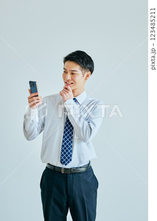 あごに手を当ててスマホを持つ20代の若い男性 123485211