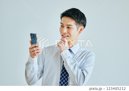 あごに手を当ててスマホを持つ20代の若い男性 123485212