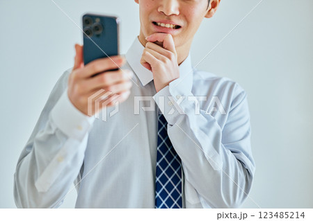 あごに手を当ててスマホを持つ20代の若い男性 123485214