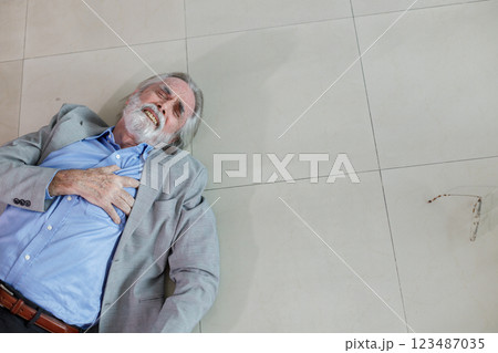 Elderly white man has an accident, falls down, lies on the floor, hands on chest, chest pain, heart disease, heart failure. 123487035