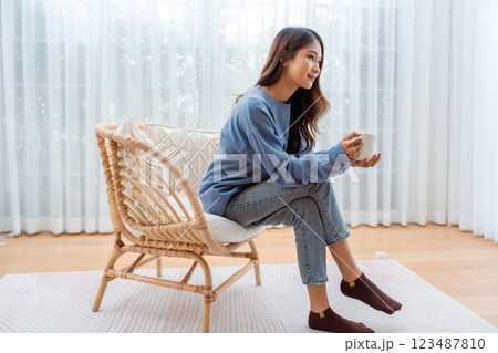 Young Asian woman happy and smiling, sitting on seat and holding mug in living room at home 123487810