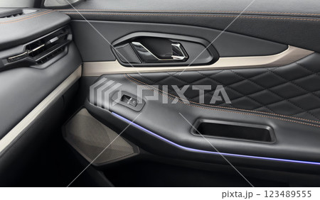 Door handle with power window control buttons. Black perforated leather interior with stitching. Modern car black leather interior details. Door handle with power window control buttons. Black perforated leather interior with stitching. Modern car black leather interior details. 123489555