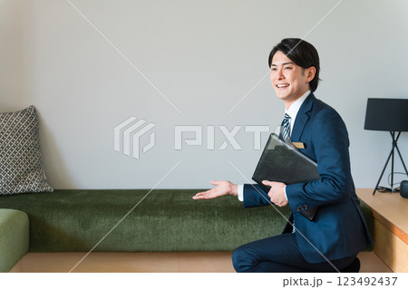 モデルハウスのリビングでソファを案内・提案するスーツ姿のハウスメーカーの若い男性営業マン モデルハウスのリビングでソファを案内・提案するスーツ姿のハウスメーカーの若い男性営業マン 123492437