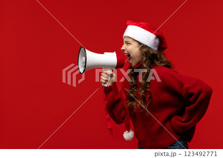 Energetic girl in Santa hat and sweater shouts into megaphone 123492771