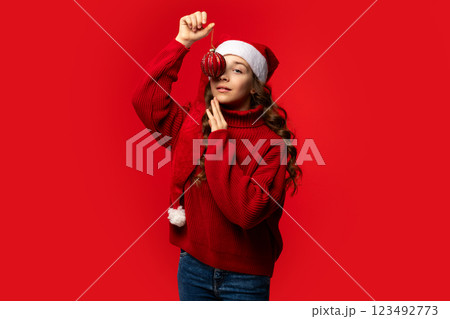 Teen girl in Santa hat posing with red Christmas ornament. 123492773