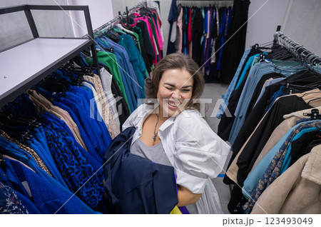 Top view of a chubby-cheeked woman holding an armful of clothes in a plus size store.  123493049