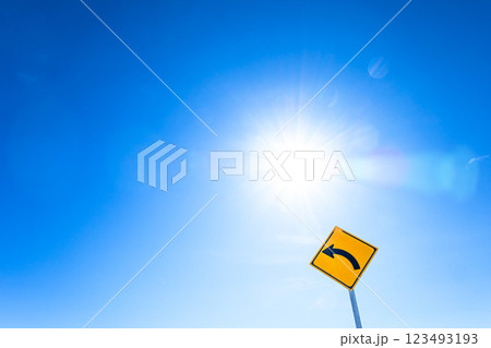 青空と太陽の光をバックに左折のカーブの標識があるイメージ風景 青空と太陽の光をバックに左折のカーブの標識があるイメージ風景 123493193
