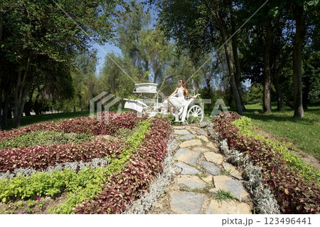 Woman in White Dress Sitting on Carriage in Garden  123496441