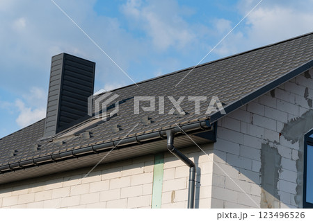 The modern house showcases a newly installed tiled roof, complemented by a sleek chimney structure under bright, sunny skies, enhancing its architectural elegance The modern house showcases a newly installed tiled roof, complemented by a sleek chimney structure under bright, sunny skies, enhancing its architectural elegance 123496526