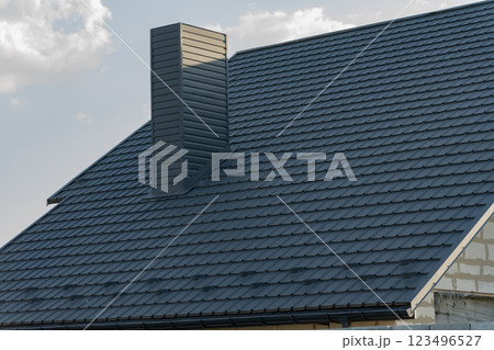 The contemporary house roof showcases a stylish tiled design with a prominent chimney, surrounded by a peaceful atmosphere and blue skies 123496527
